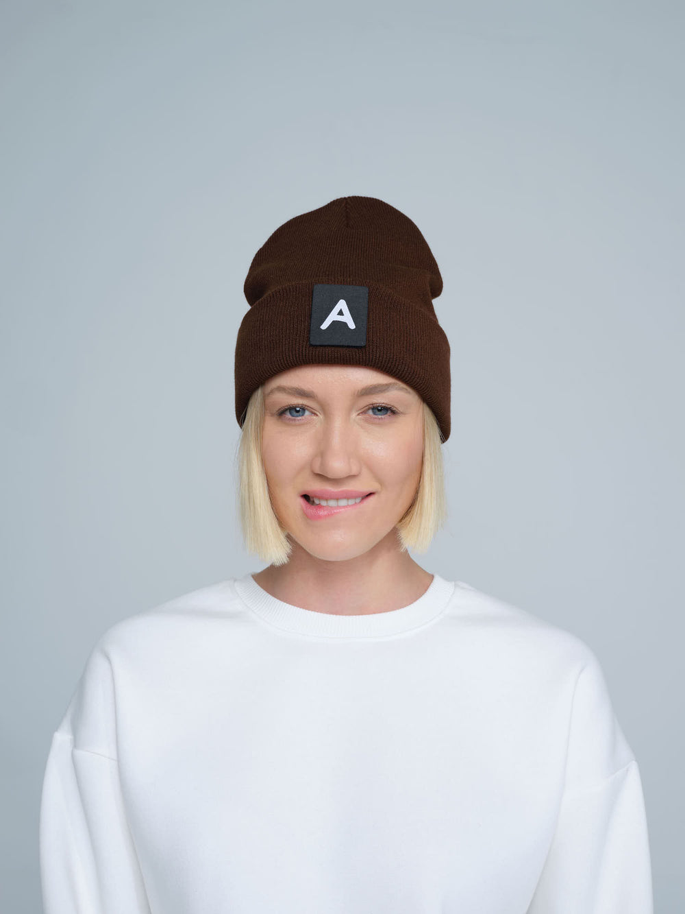 A person wearing a dark brown beanie with a 'A' letter design patch on the front.