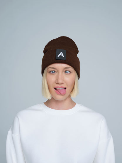 A person wearing a dark brown beanie with a 'A' letter design patch on the front.