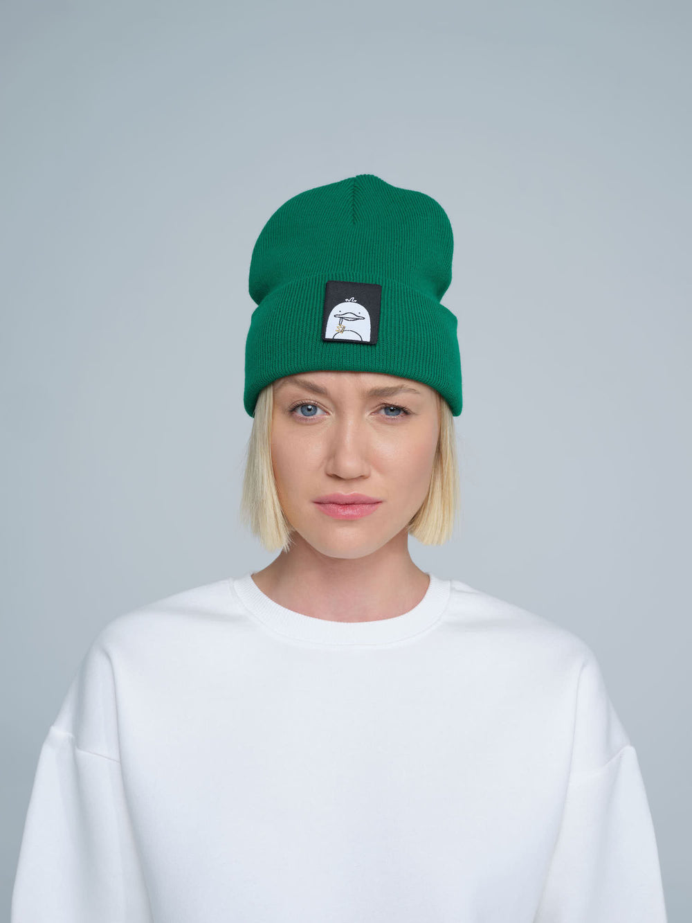 female model wearing dark green beanie with a 'duck' patch on the front