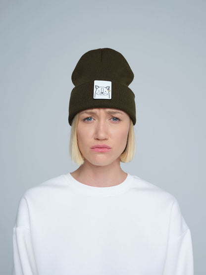 A person wearing a dark olive green beanie with a 'fox' design on the cuff, paired with a white t-shirt.