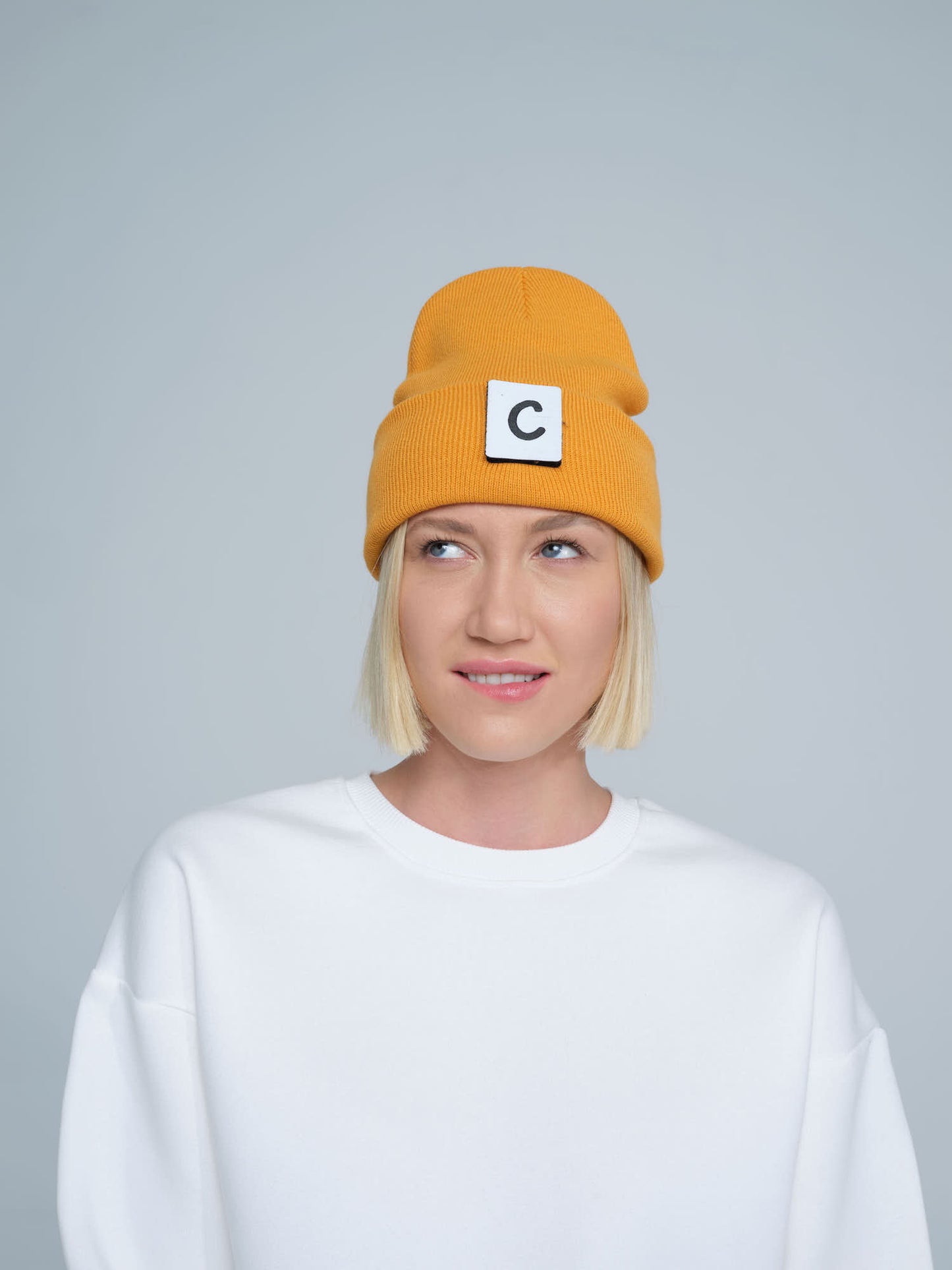 A person wearing a dark orange beanie with a design on the fold, and a letter 'C' logo on the forehead area.