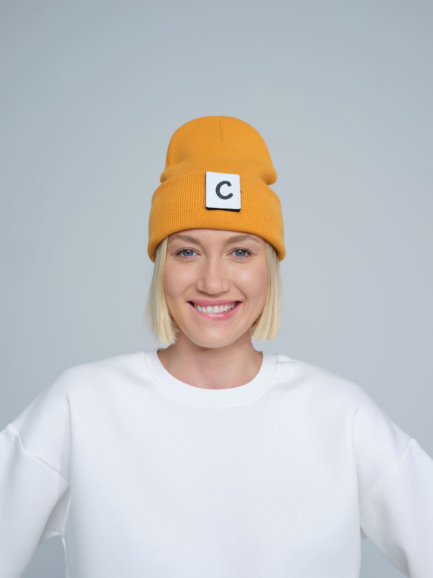 A person wearing a dark orange beanie with a design on the fold, and a letter 'C' logo on the forehead area.
