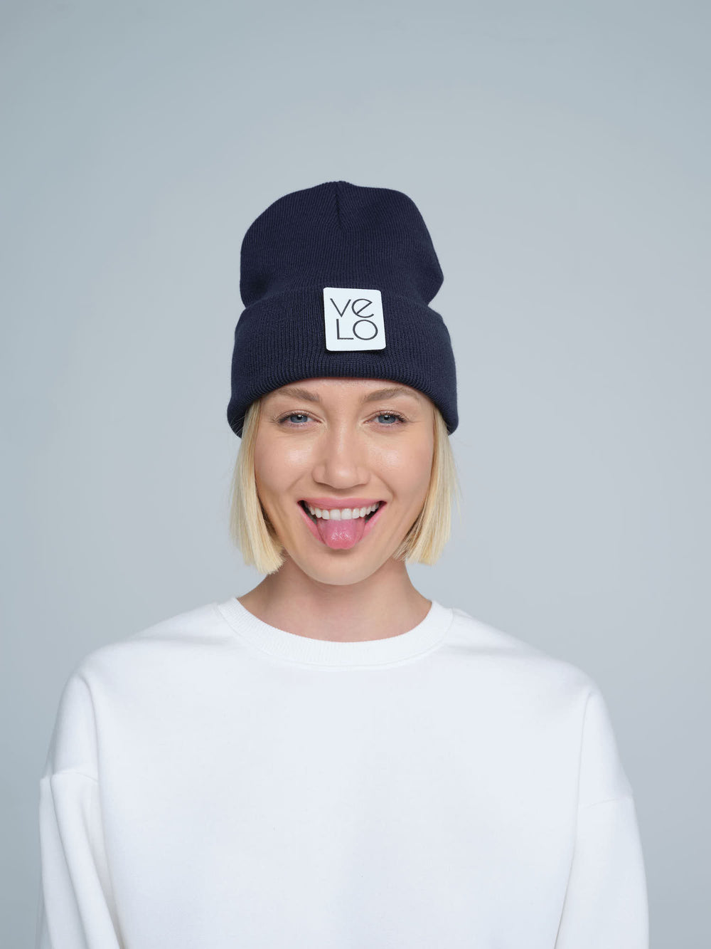 A woman wearing a dark slate navy beanie with a design on the cuff, and the brand logo 'Velo' on the fold.