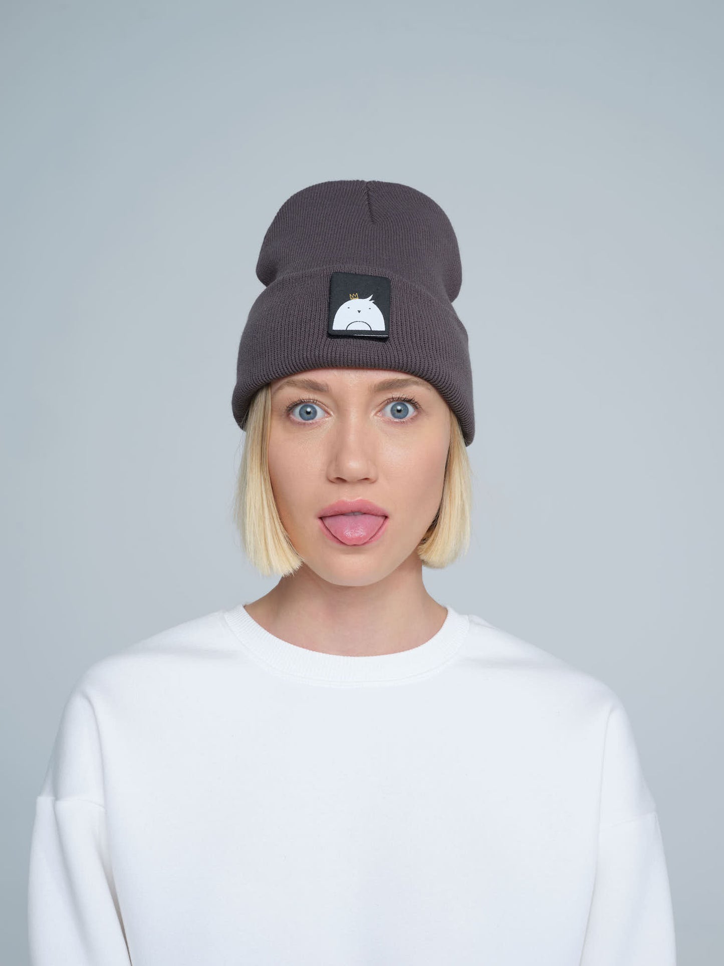 A person wearing a dim gray beanie hat with a 'bird' design patch on the front.