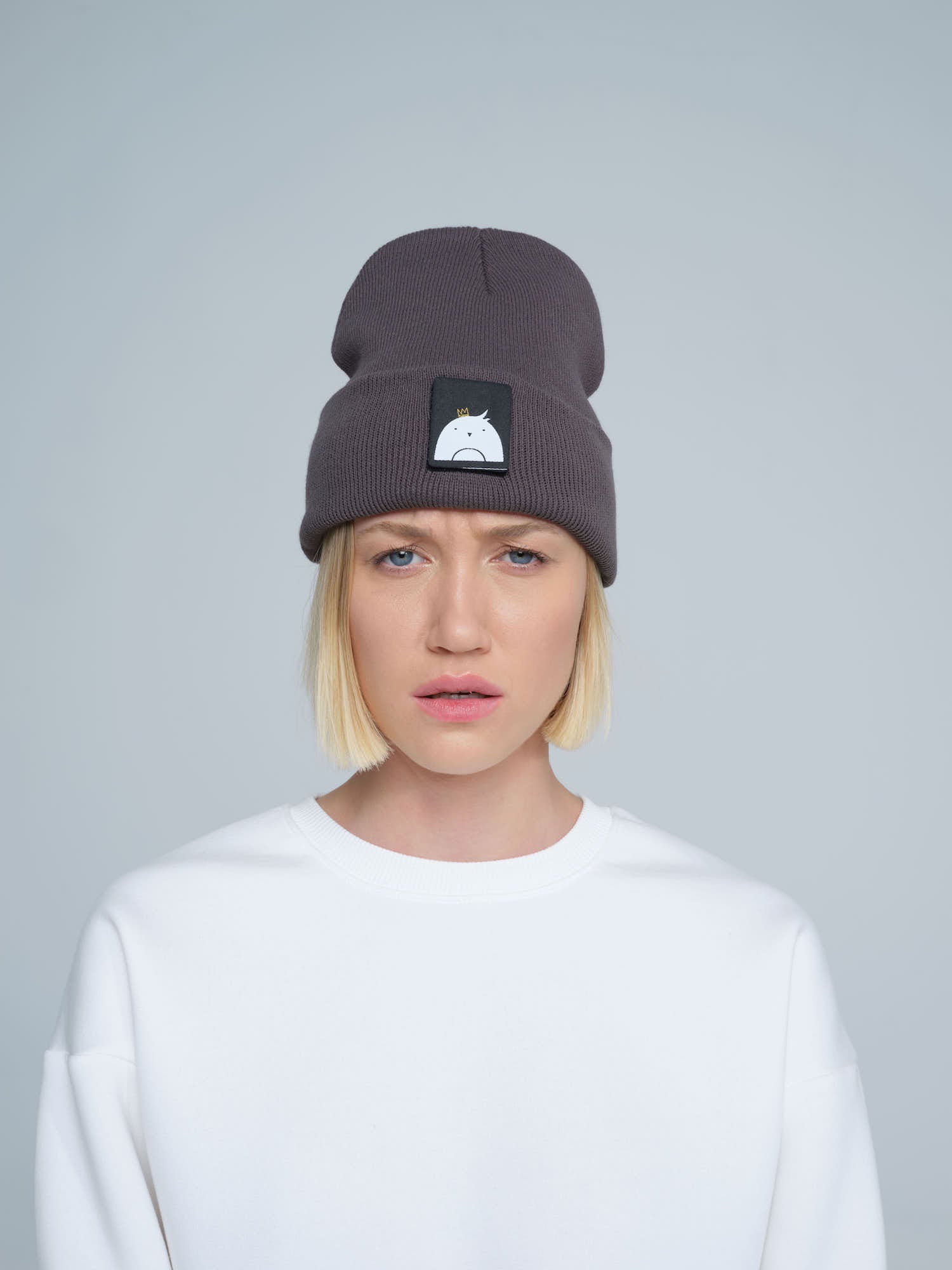 A person wearing a dim grey beanie hat with a 'bird' design patch on the front.