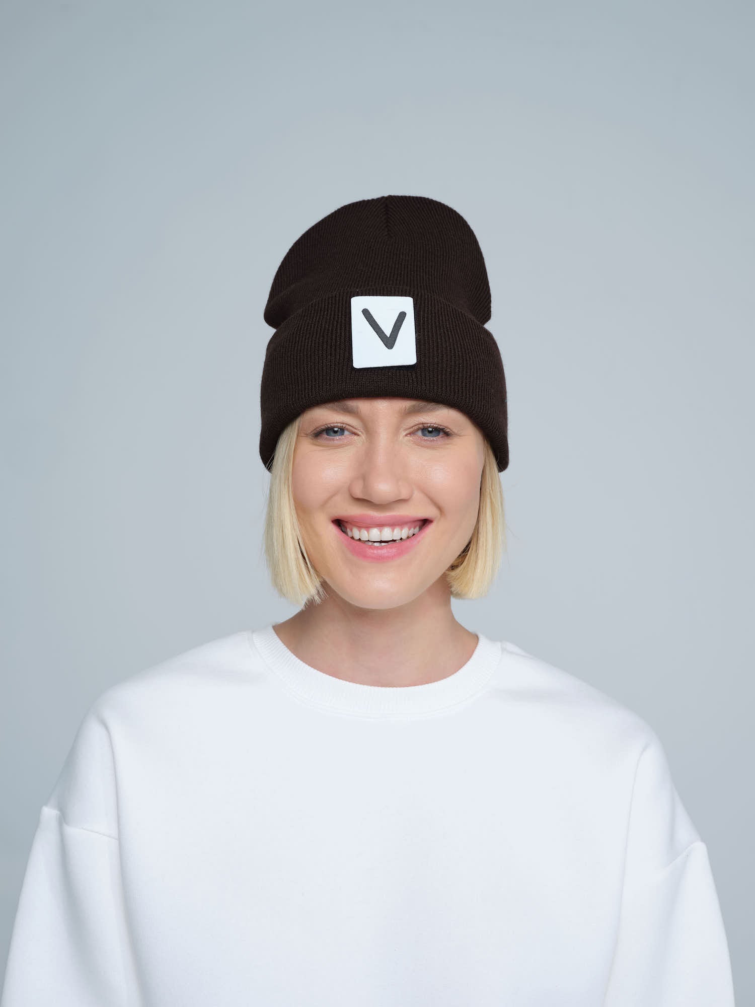A person wearing an espresso beanie hat with a 'V' letter design on the cuff, and a white t-shirt.