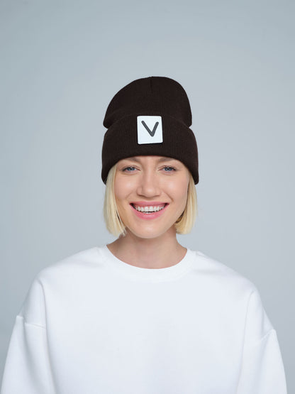 A person wearing an espresso beanie hat with a 'V' letter design on the cuff, and a white t-shirt.