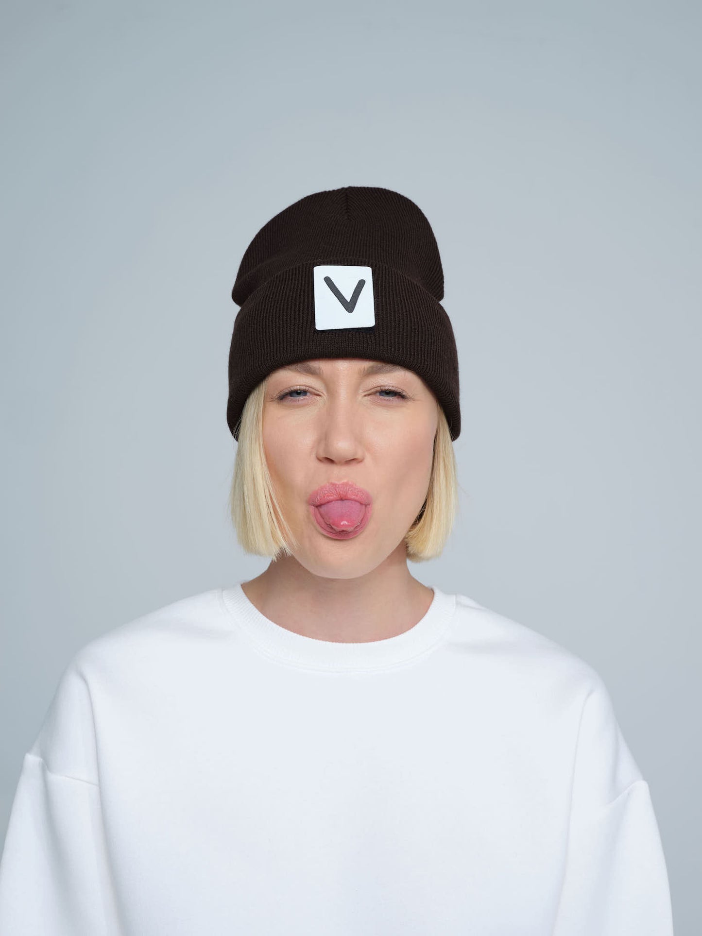 A person wearing an espresso beanie hat with a 'V' letter design on the cuff, and a white t-shirt.