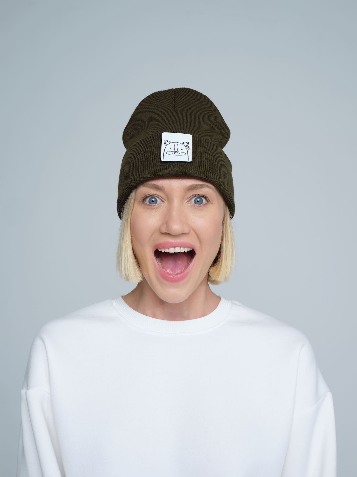 A person wearing a forest green beanie with a design on the cuff, paired with a white t-shirt.