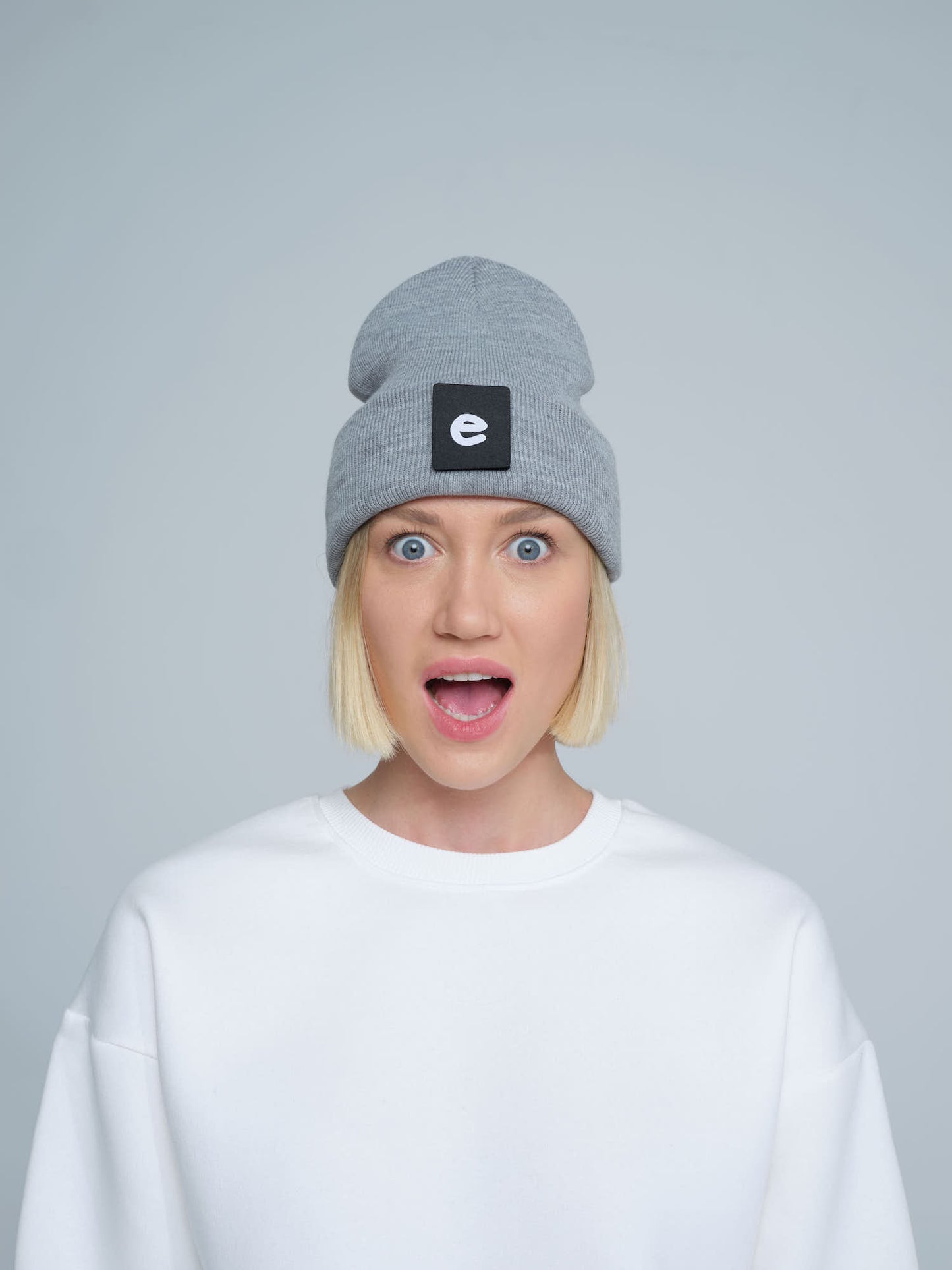 female model wearing grey beanie with 'e' letter design patch on the front