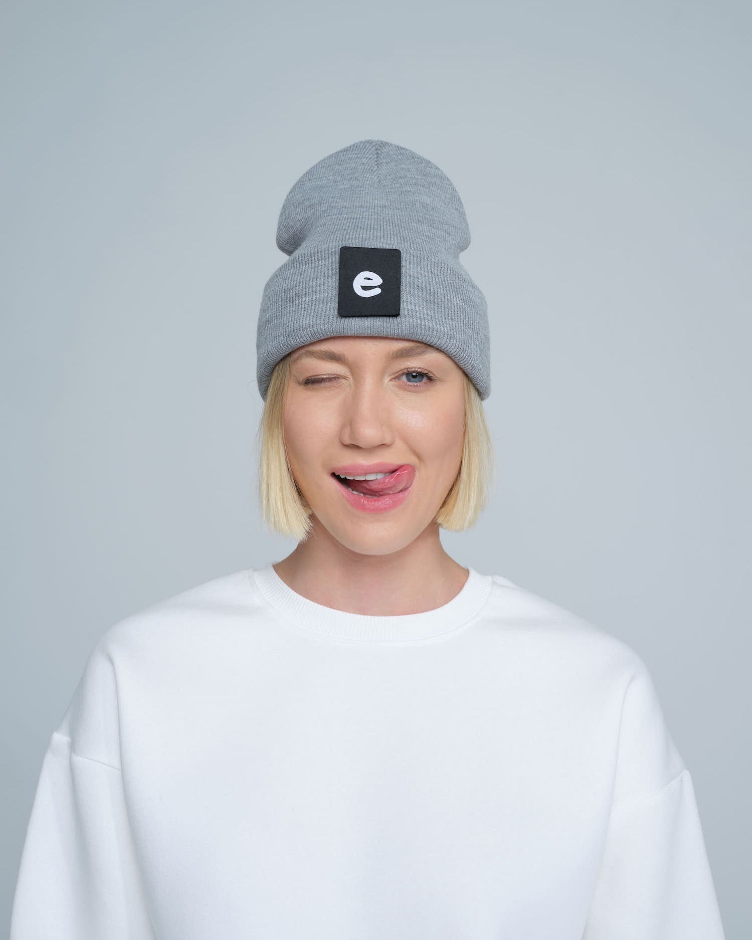 female model wearing grey beanie with 'e' letter design patch on the front