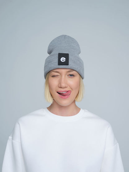 female model wearing grey beanie with 'e' letter design patch on the front