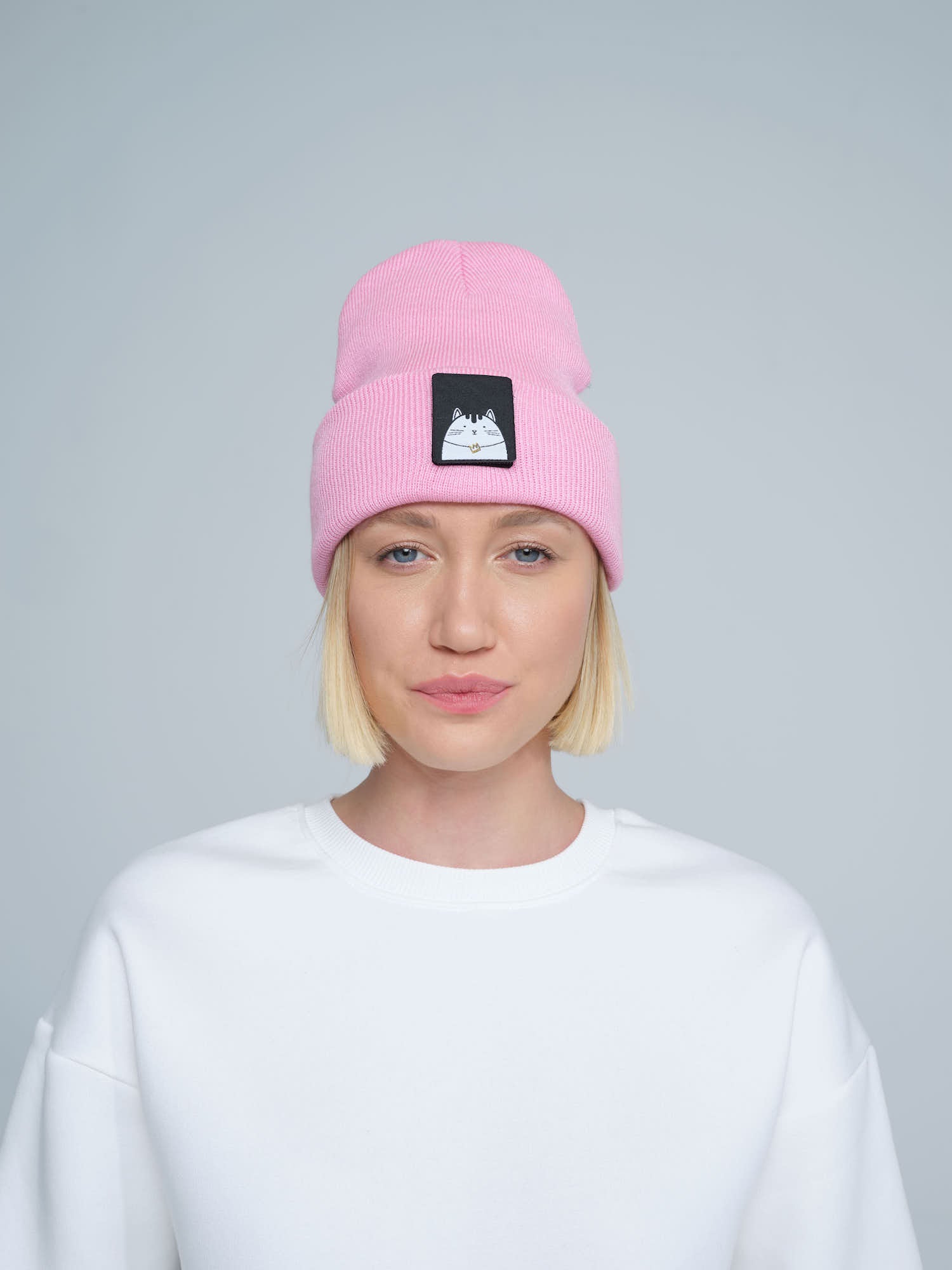 A person wearing a pink beanie with a cat design patch on the front.