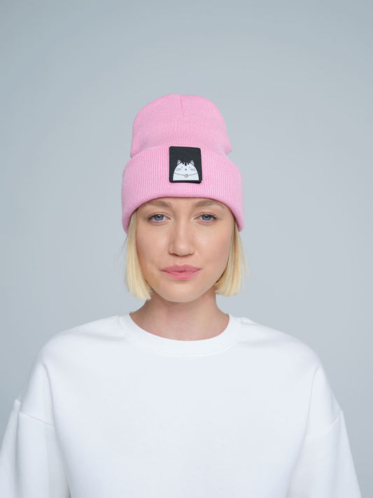 A person wearing a pink beanie with a cat design patch on the front.