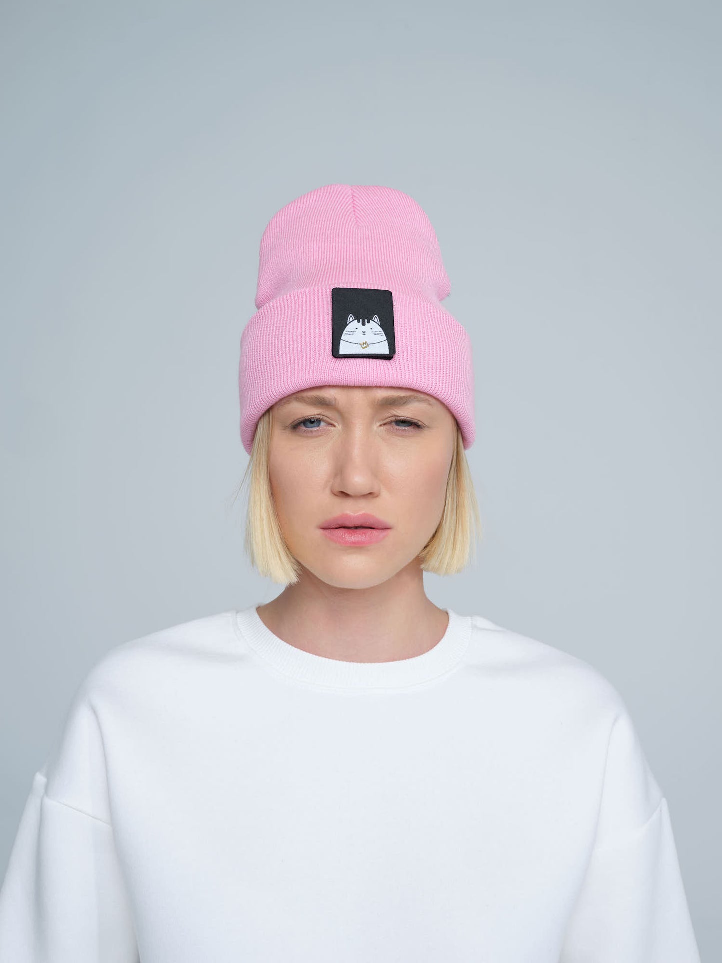 A person wearing a pink beanie with a cat design patch on the front.