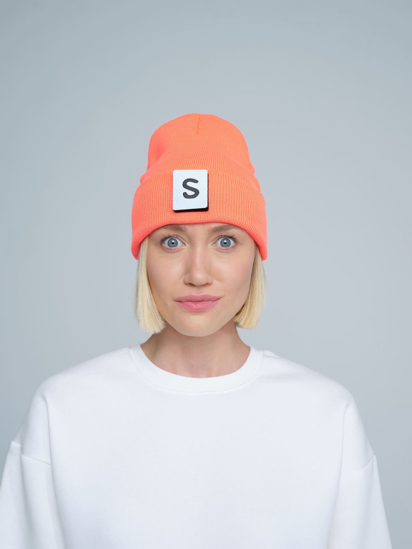 A person wearing a neon orange beanie with a text pattern on the fold, paired with a white t-shirt.