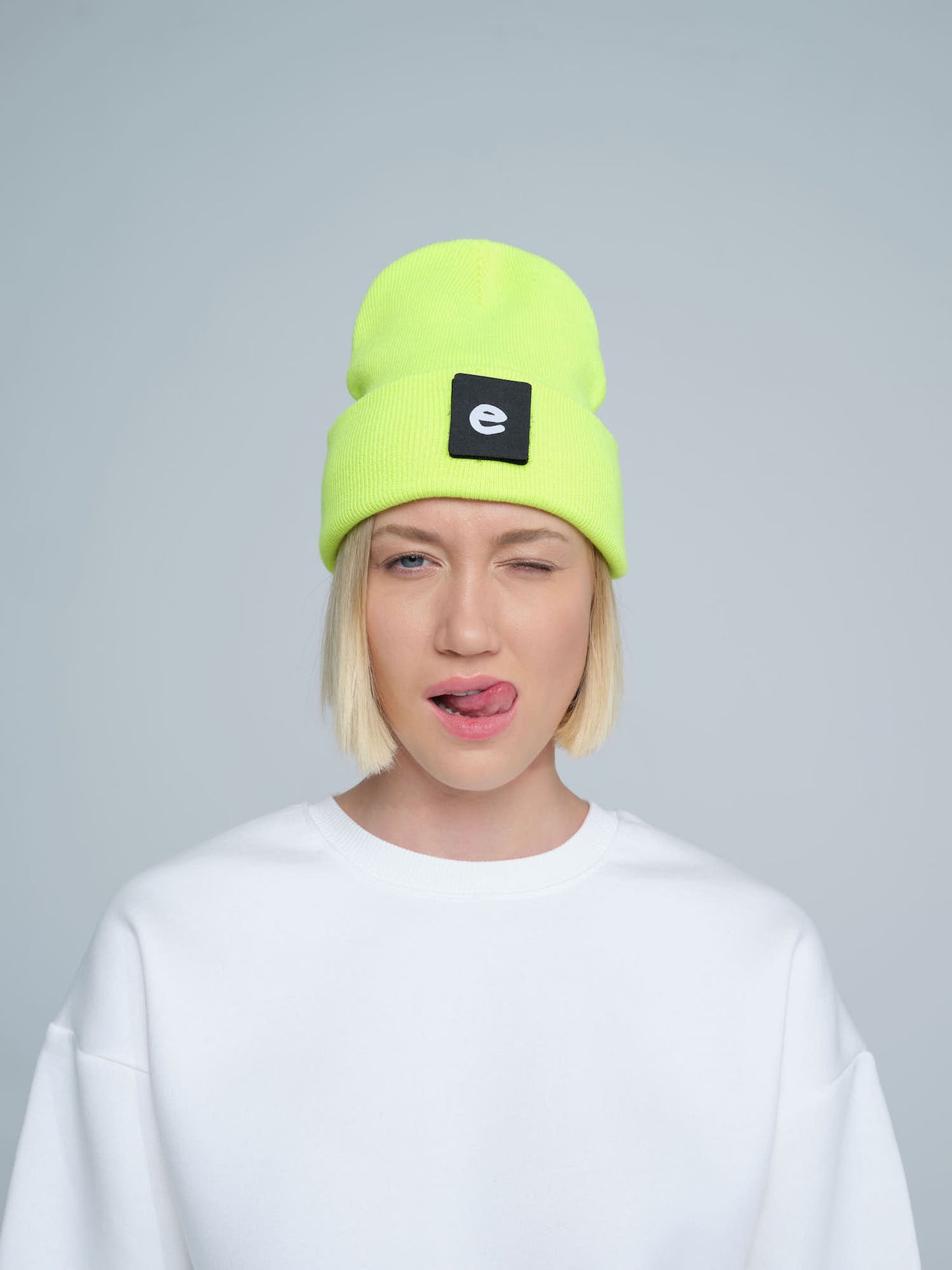 female wearing neon yellow beanie with a 'e' letter patch on it with a cute face