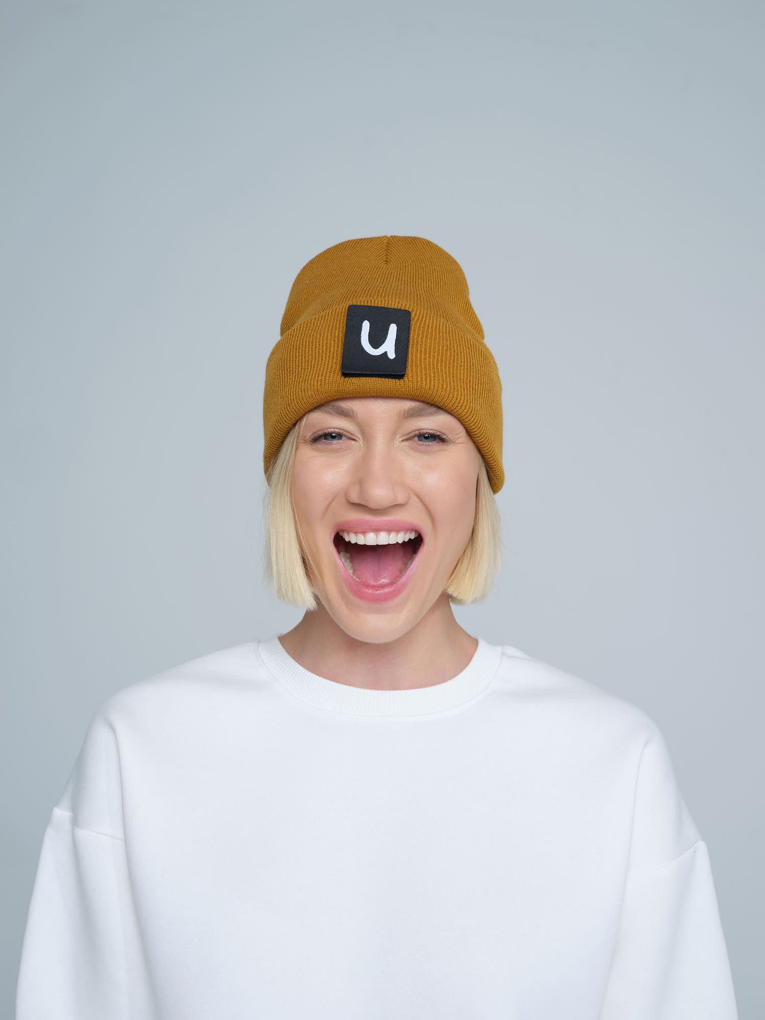 female model wearing peru colour patch ready beanie with 'u' letter on it and smiling