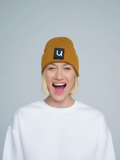 female model wearing peru colour patch ready beanie with 'u' letter on it and smiling