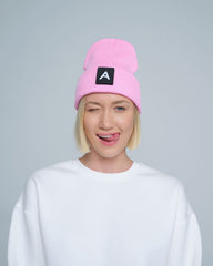 A person wearing a pink beanie with a design on top and the letter 'A' on it, paired with a white crew neck sweater.