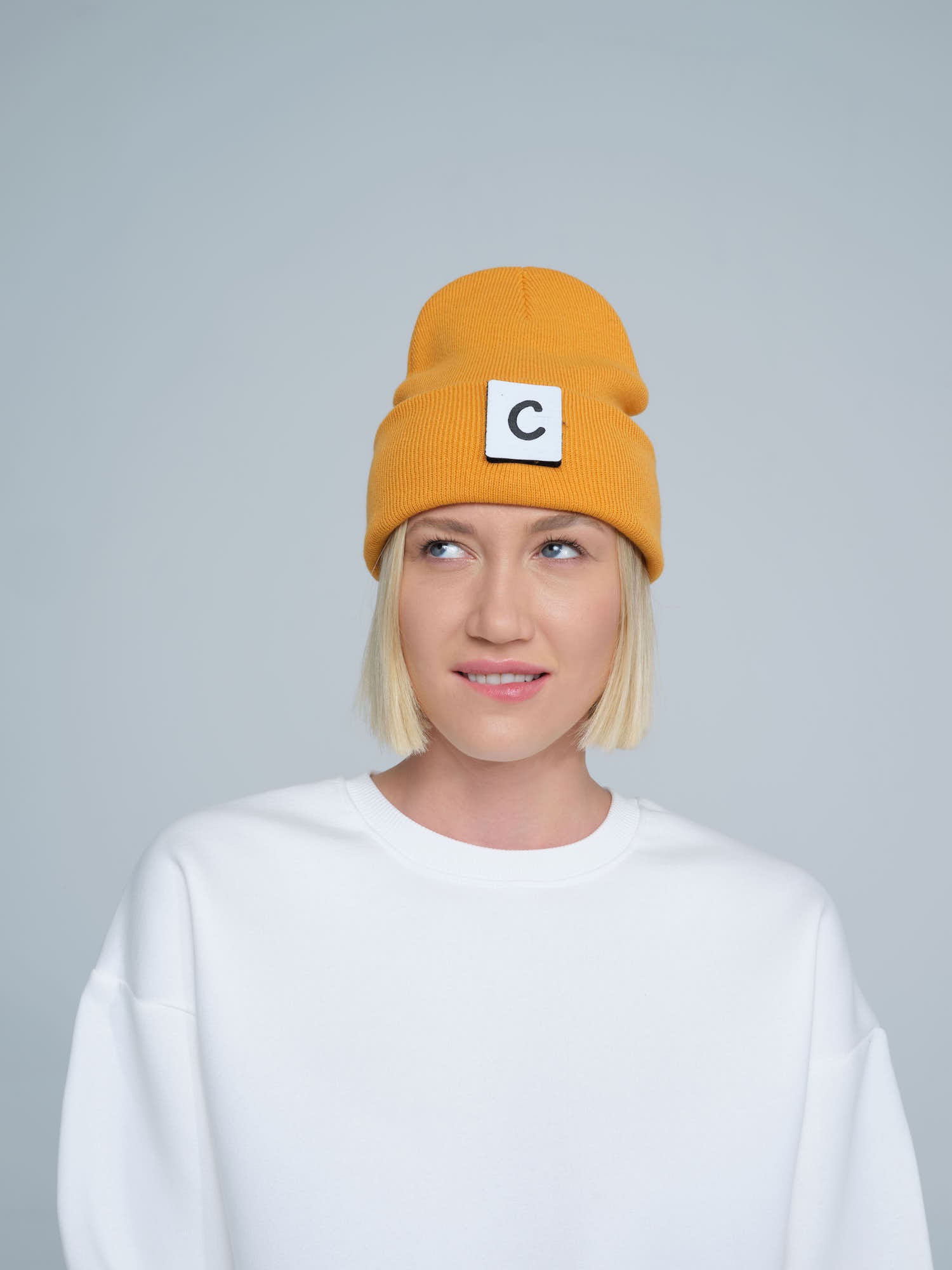 A person wearing a pumpkin beanie with a design on the fold, and a letter 'C' logo on the forehead area.