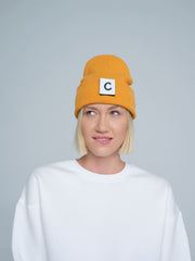 A person wearing a pumpkin beanie with a design on the fold, and a letter 'C' logo on the forehead area.