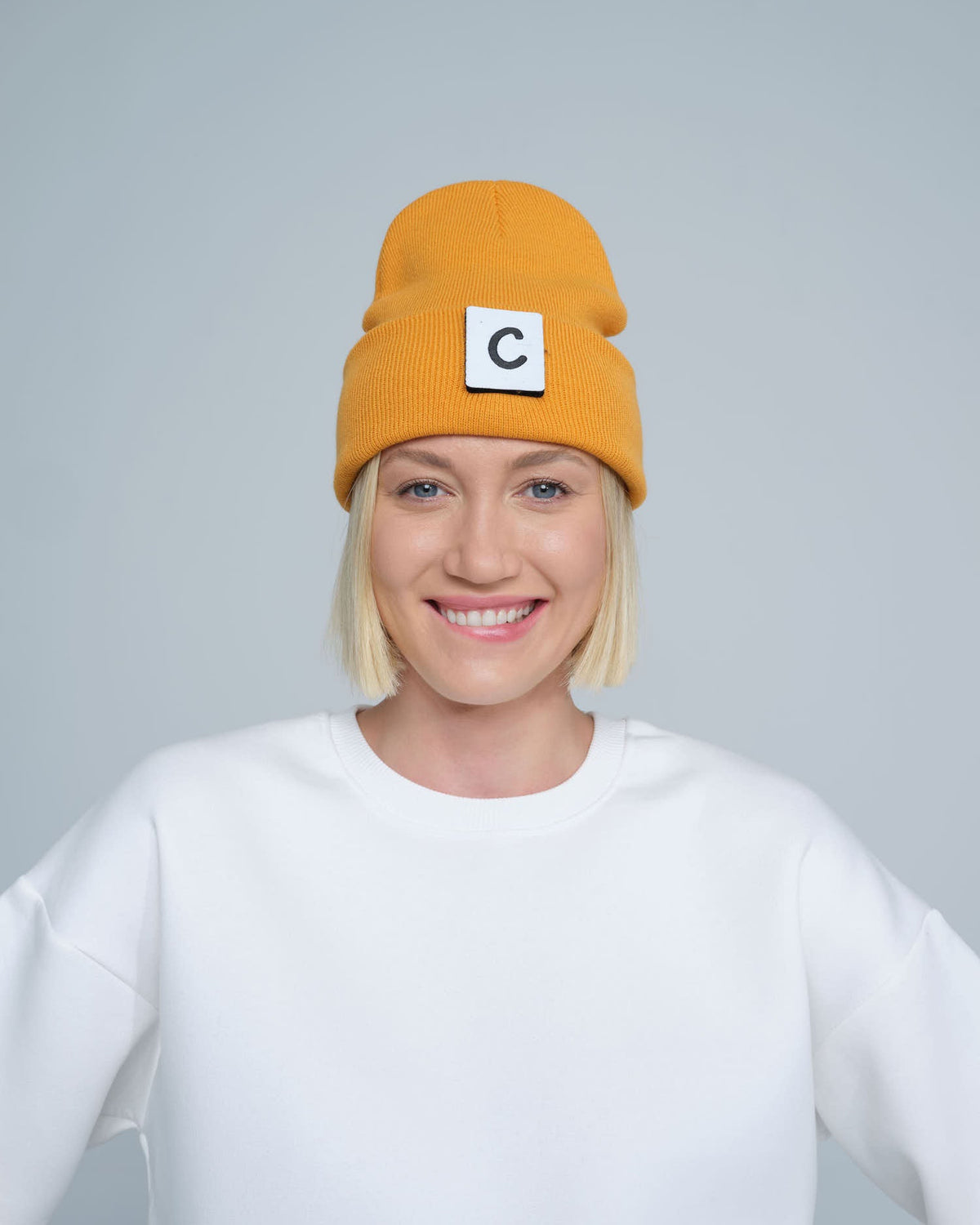 A person wearing a pumpkin beanie with a design on the fold, and a letter 'C' logo on the forehead area.
