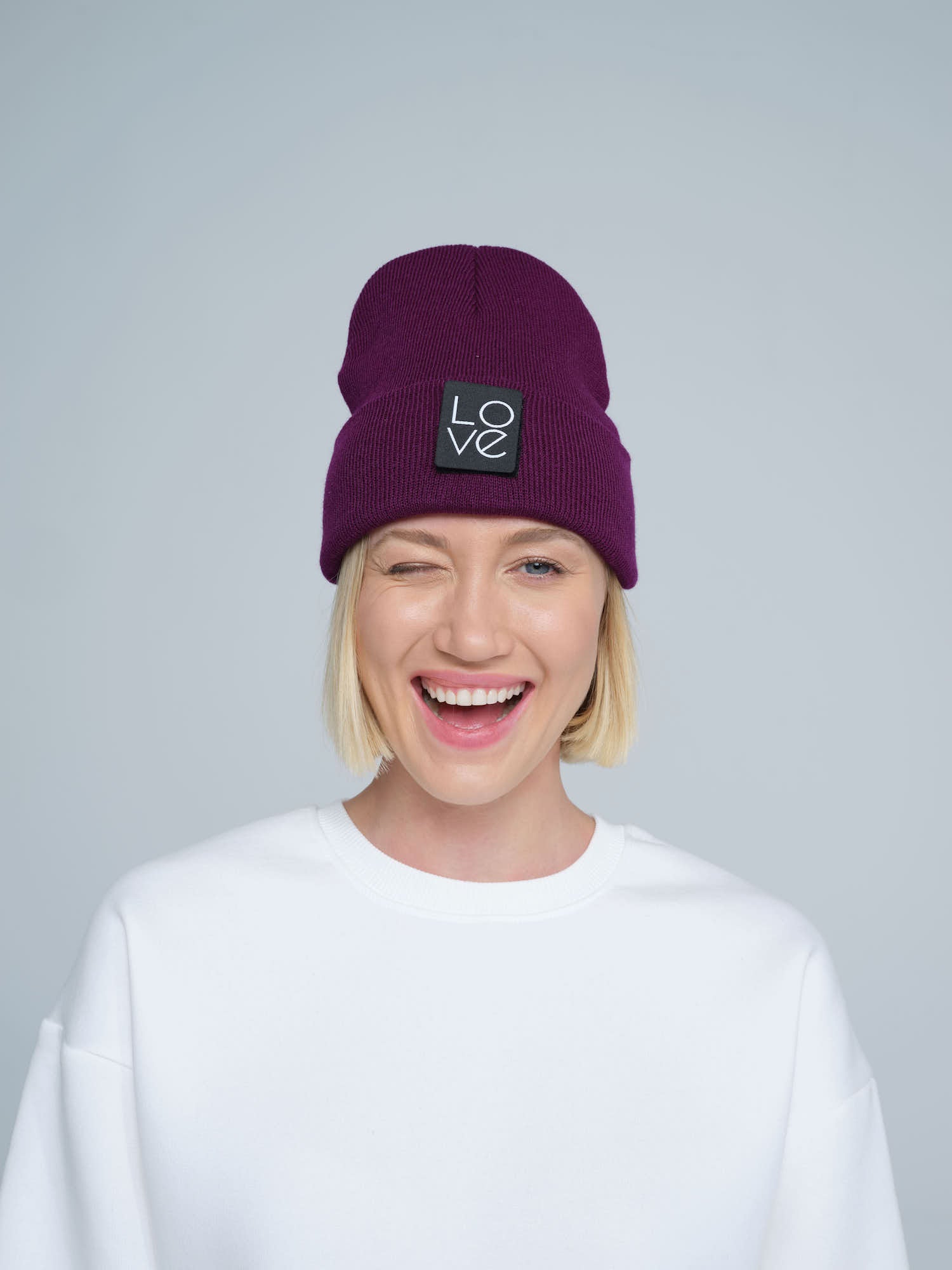 A person wearing a purple beanie hat with a 'Love' logo on the front with a smiling face.