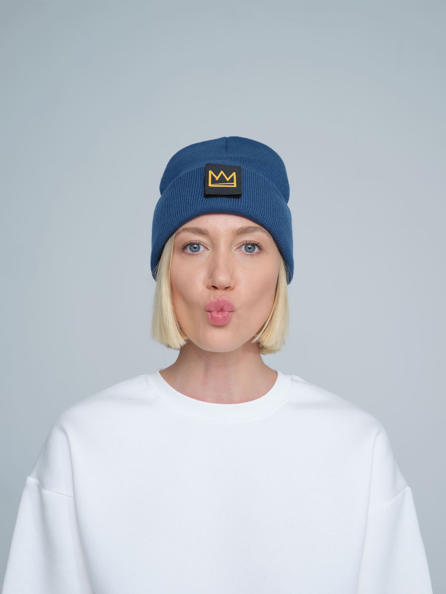 female model wearing steel blue beanie with a crown patch on it with a funny face