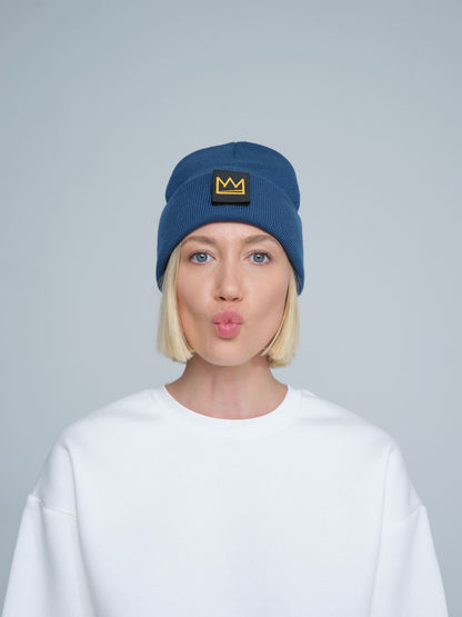 female model wearing steel blue beanie with a crown patch on it with a funny face
