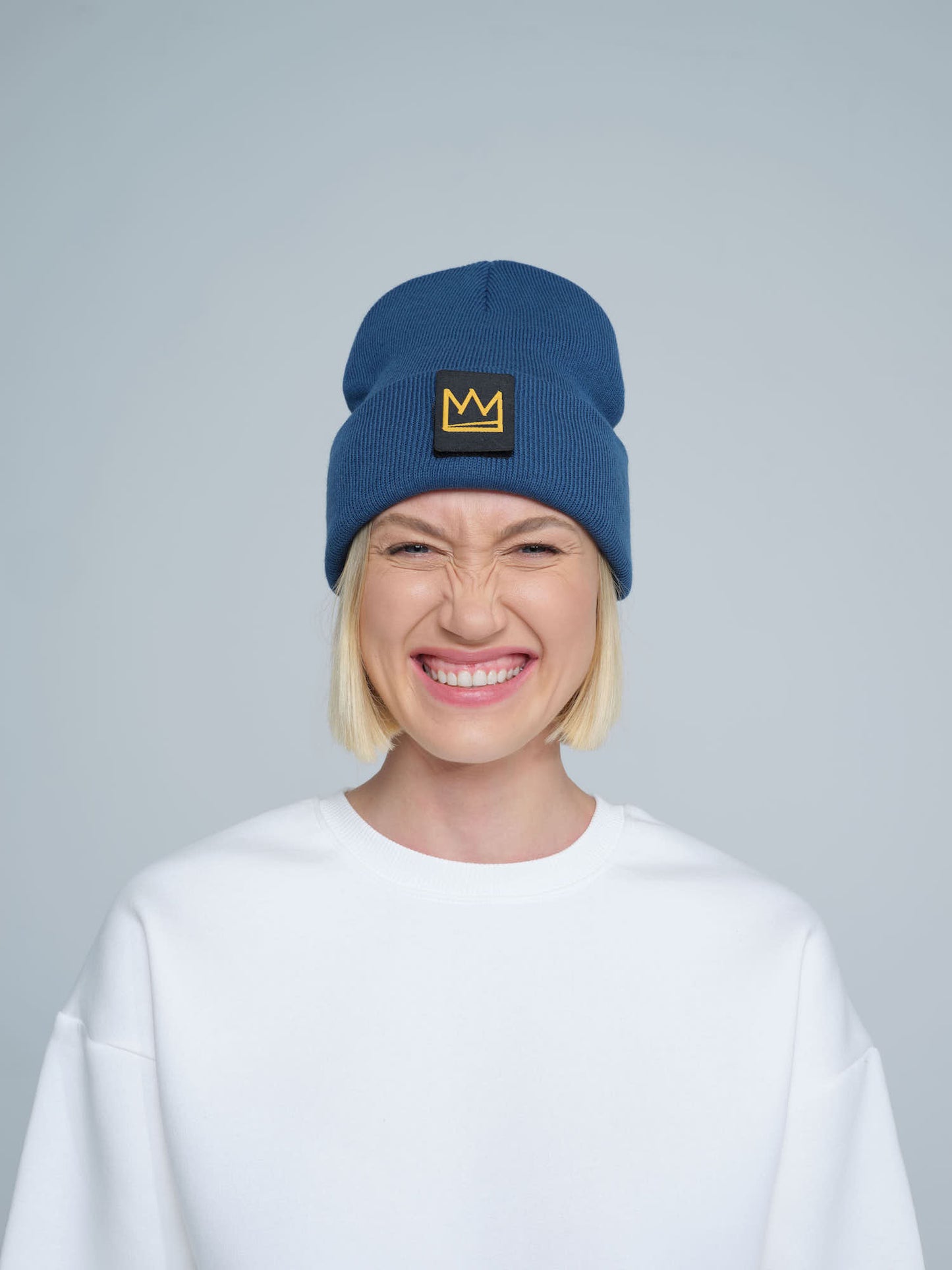 female model wearing steel blue beanie with a crown patch on it