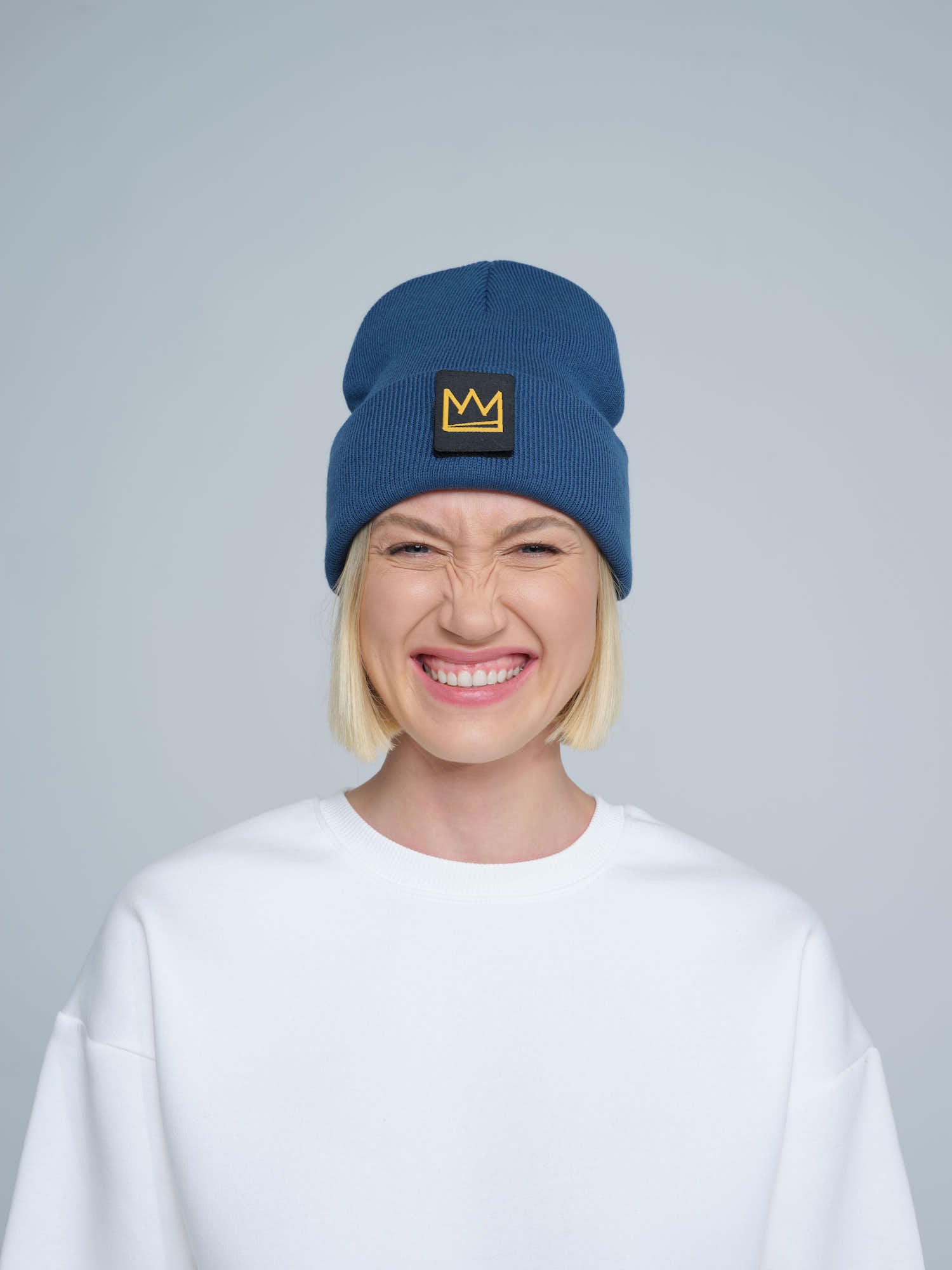 female model wearing steel blue beanie with a crown patch on it