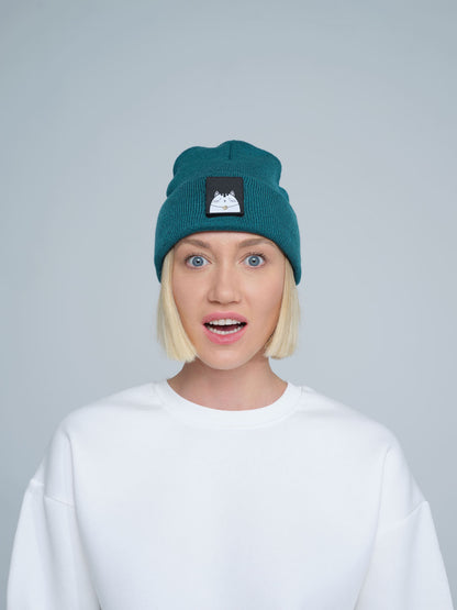 A person wearing a teal green beanie hat with a cat design on the cuff, paired with a white t-shirt.