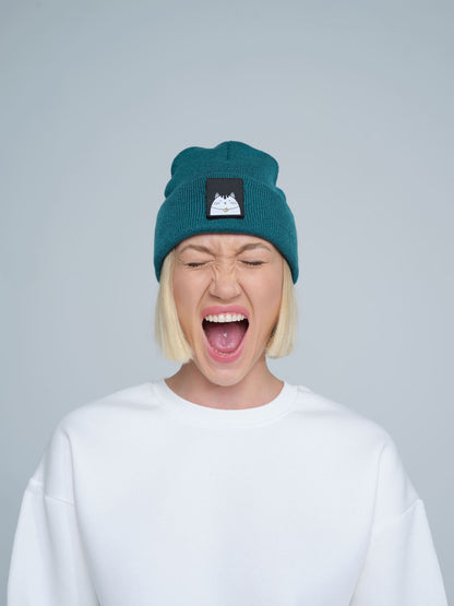 A female wearing a teal green beanie hat with a cat design on the cuff, making a scream face. 